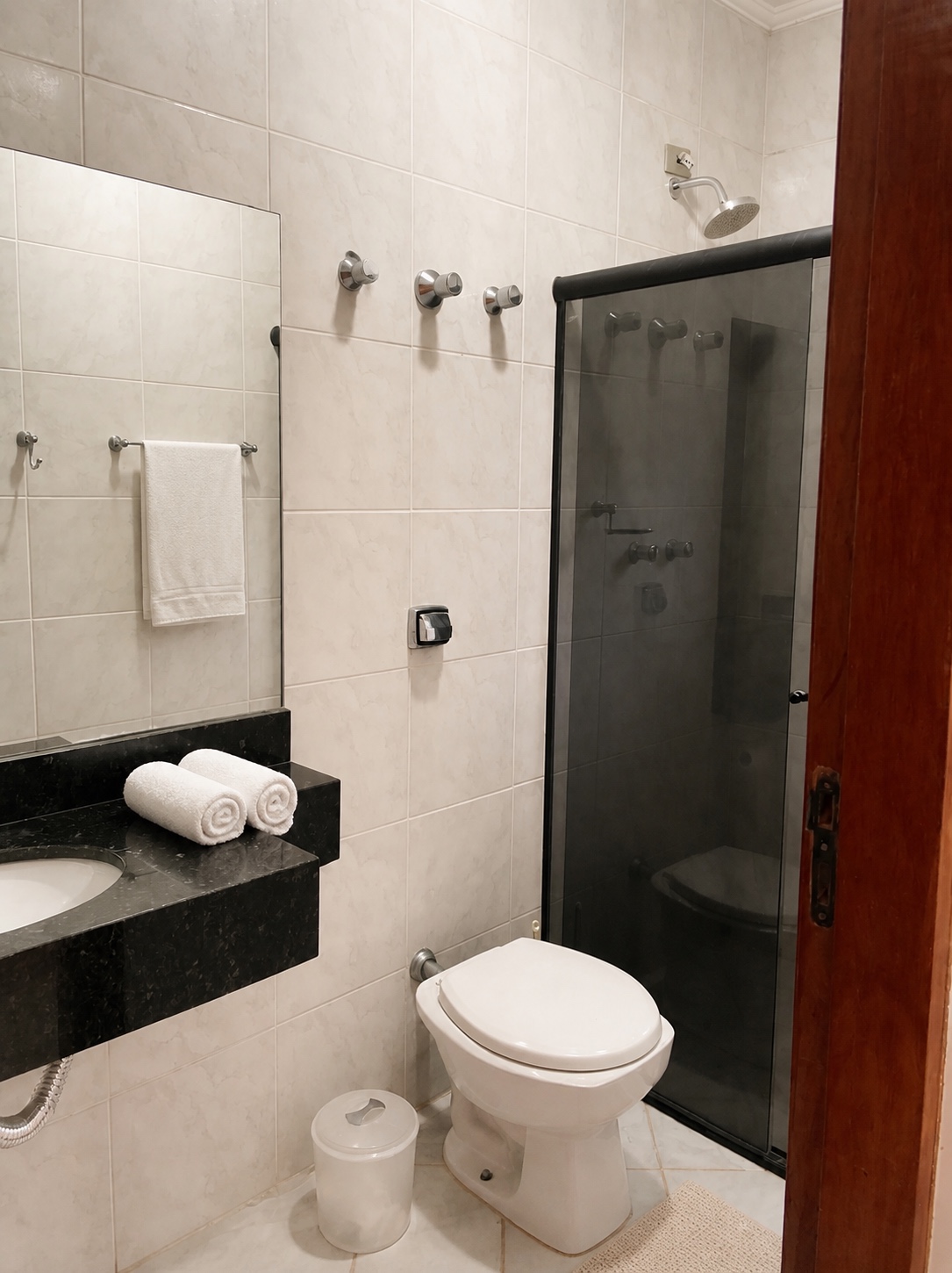 Banheiro completo da Suíte 2 com chuveiro de vidro, vaso e vanity em granito preto