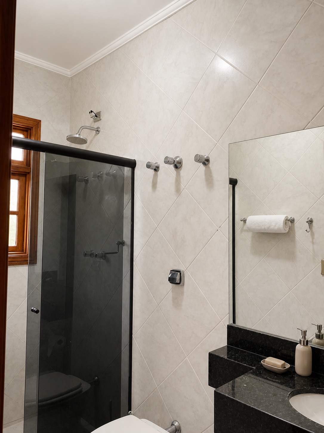 Chuveiro em mármore branco com porta de madeira ao lado e luz natural pela janela
